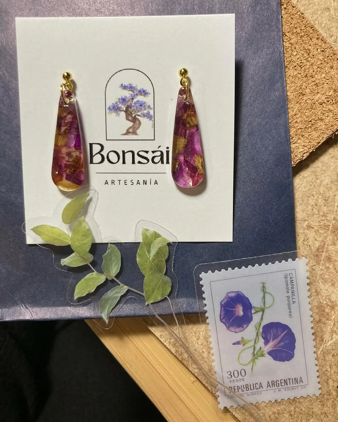 Pendientes largos de resina con flores moradas sobre la tarjeta del taller